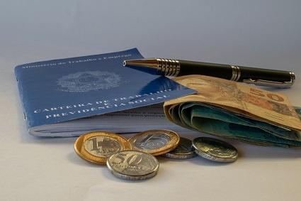 Uma caneta sobre uma carteira de trabalho e algumas notas de real com moedas