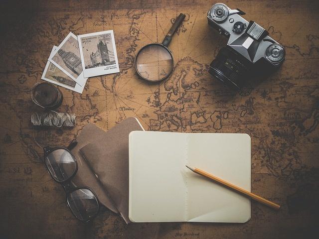 Mapa com camera fotografica, lupa, óculos, fotografias, bloco de notas e lápis sobre a mesa