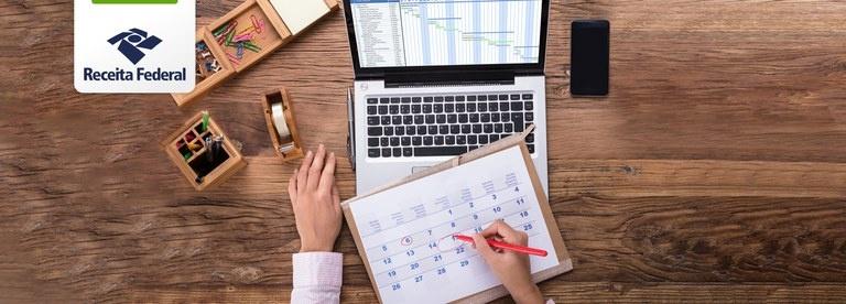 Homem escrevendo no calendário em frente ao notebook