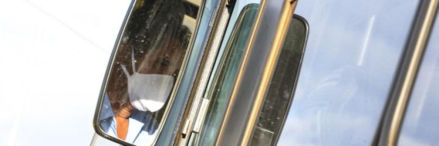 Reflexo de motorista com máscara em retrovisor de ônibus