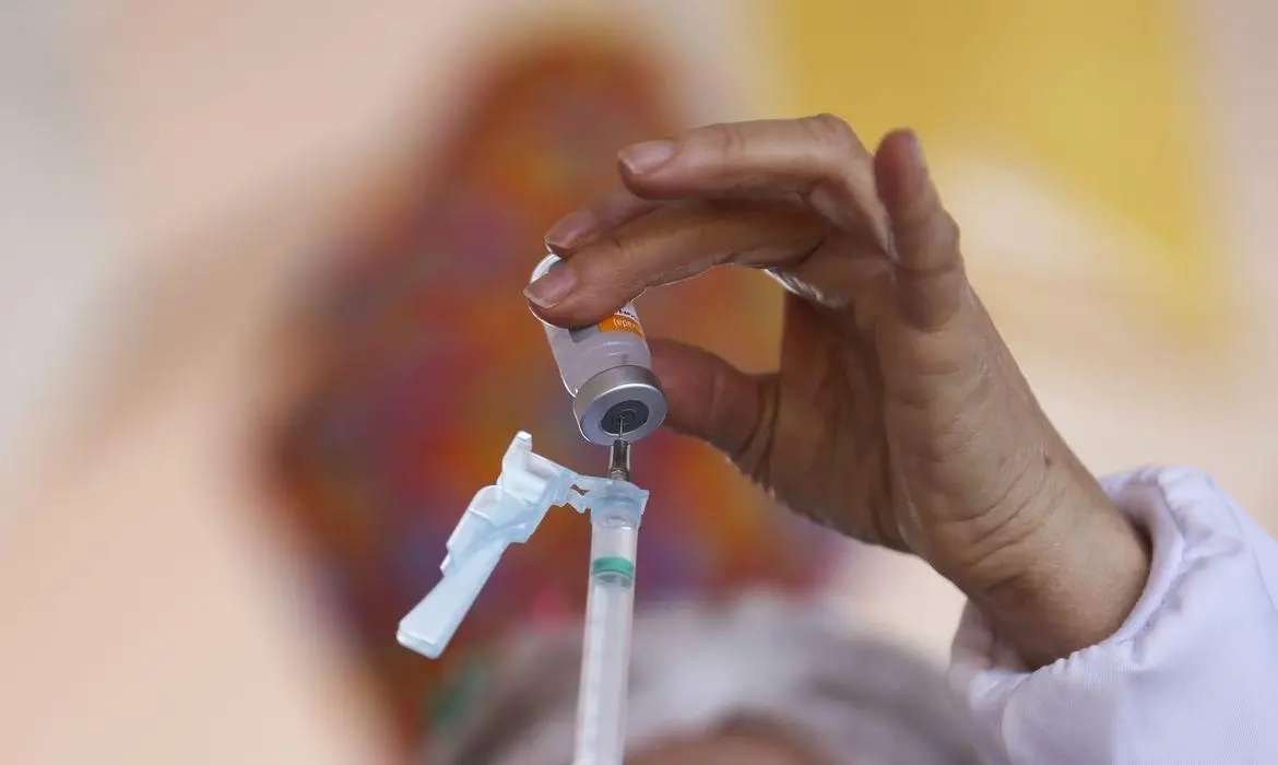Mãos enchendo seringa com vacina