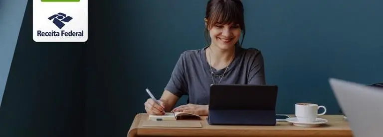 Mulher escrevendo no bloco de notas em frente ao notebook