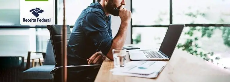 Homem sentado a frente do notebook com a mão na boca
